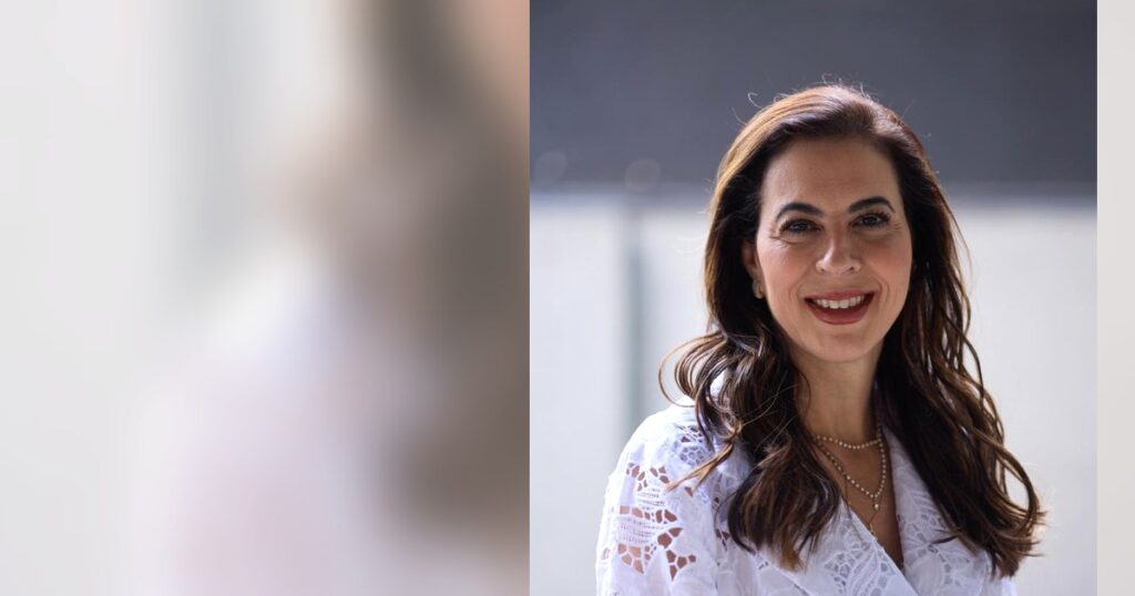Dra. Renata Mitelman, dermatologista, sorrindo à mesa do consultório, em Perdizes, São Paulo